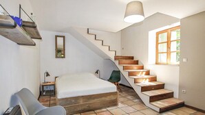 Un dormitorio con cama de madera, una silla, un escritorio, una lámpara, un espejo, una escalera y una ventana.