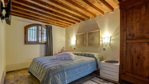 A bedroom with a wooden ceiling, a bed with a blue quilt, a nightstand, a wall-mounted lamp, and a window with curtains. - Lovely home in Castiglione della Pesc (Castiglione della Pesc)