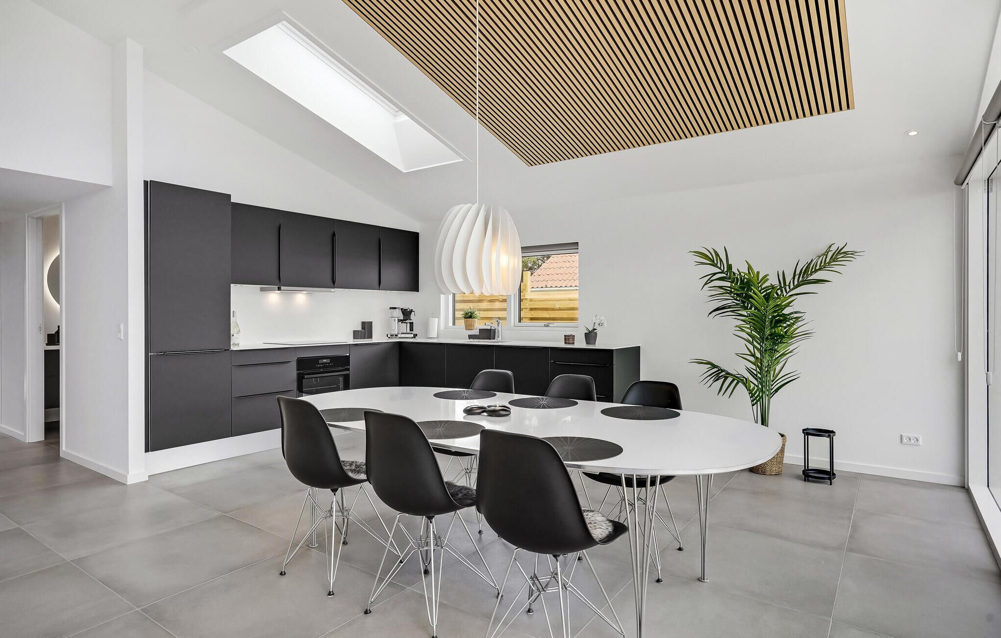 A modern kitchen with black cabinets, a white countertop, and a skylight above the dining area.