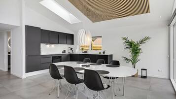 A modern kitchen with black cabinets, a white countertop, and a skylight above the dining area.