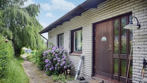 A rustic log cabin with a wooden door, a small porch, and a garden with purple flowers.