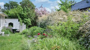 A garden with various plants and flowers, a small structure, and a building in the background.