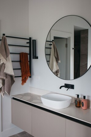 A modern bathroom with a round mirror, a white sink, and a towel rack with multiple towels. - Majuba Country Lodge (Kalgan)