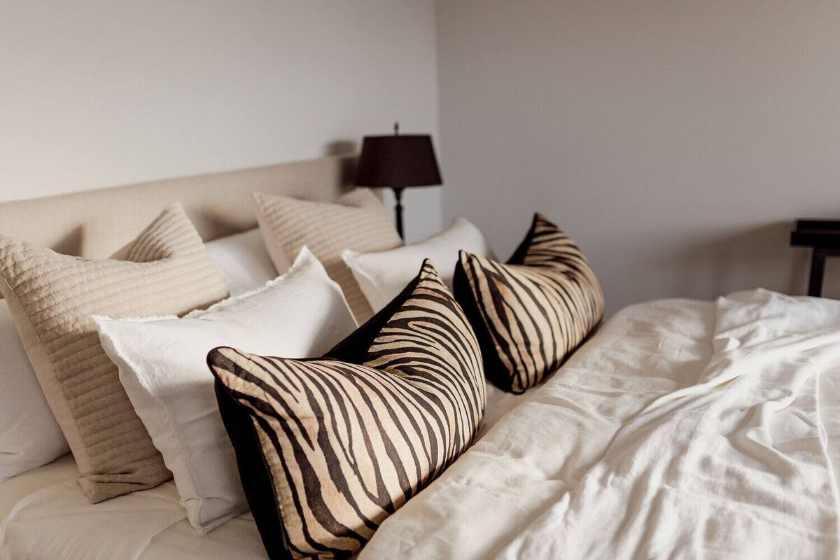 A neatly made bed with a variety of pillows, including striped and solid colors, and a lamp on a bedside table.