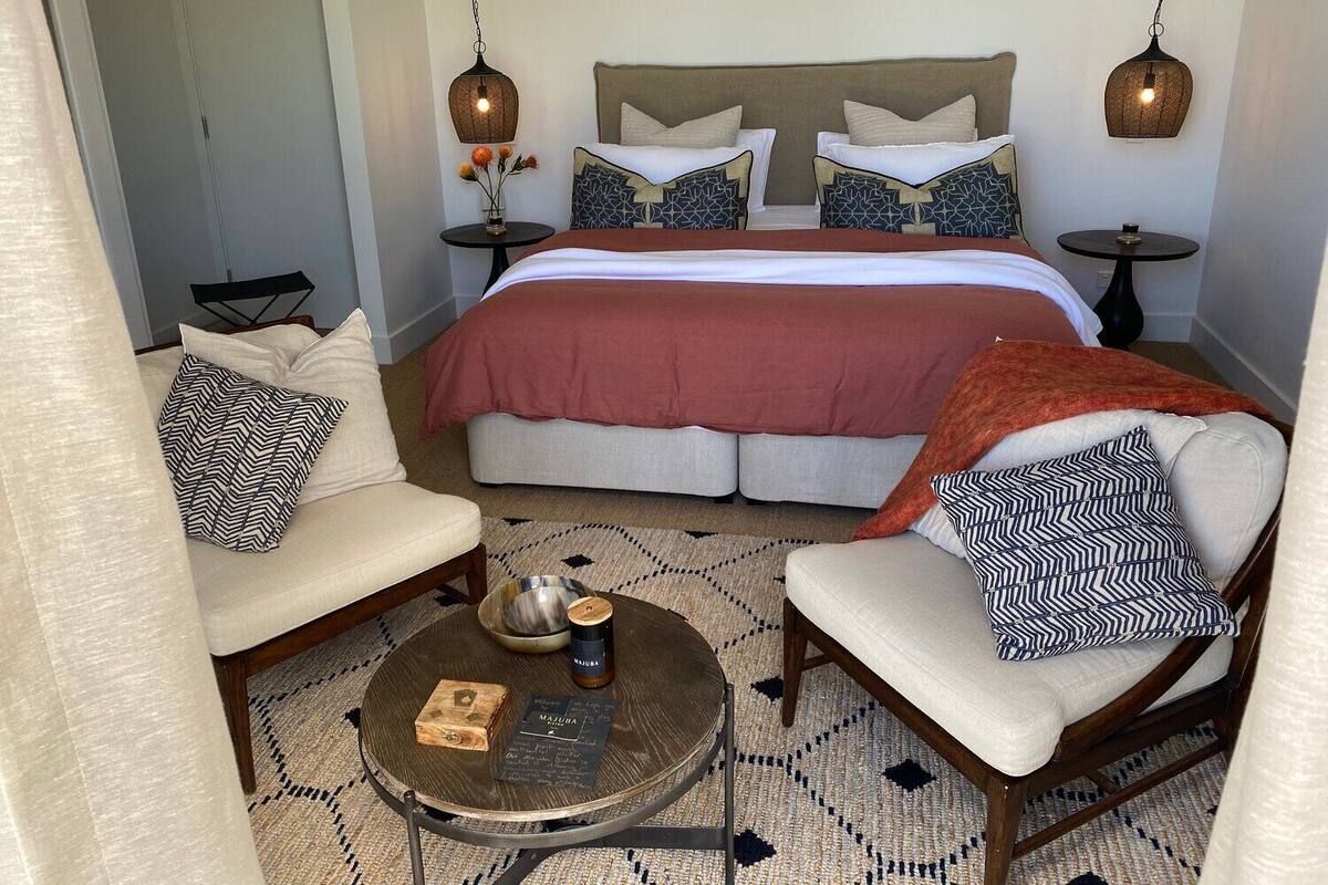 A neatly arranged bedroom with a large bed, two bedside tables, a round coffee table, and two armchairs.