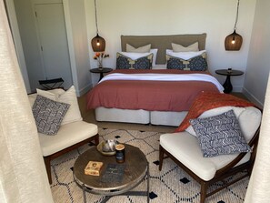 A neatly arranged bedroom with a large bed, two bedside tables, a round coffee table, and two armchairs. - Majuba Country Lodge (Kalgan)