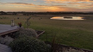 A sunset view from a deck overlooking a field with a pond and distant hills. - Majuba Country Lodge (Kalgan)