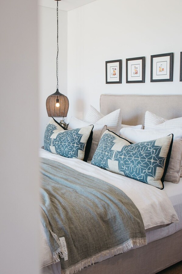 A neatly made bed with patterned pillows, a hanging light fixture, and framed artwork on the wall. - Majuba Country Lodge (Kalgan)