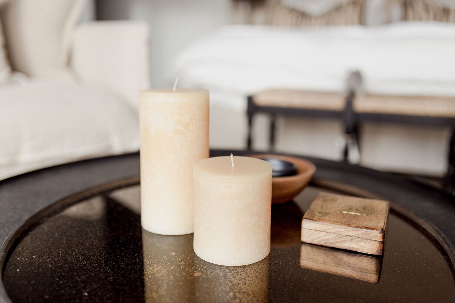 Two candles on a round table with a wooden block and a small bowl.