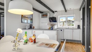 Moderni keittiö, jossa on valkoiset kaapit, suuri keittiösaareke ja ruokailutila, jossa on pöytä kahdelle.