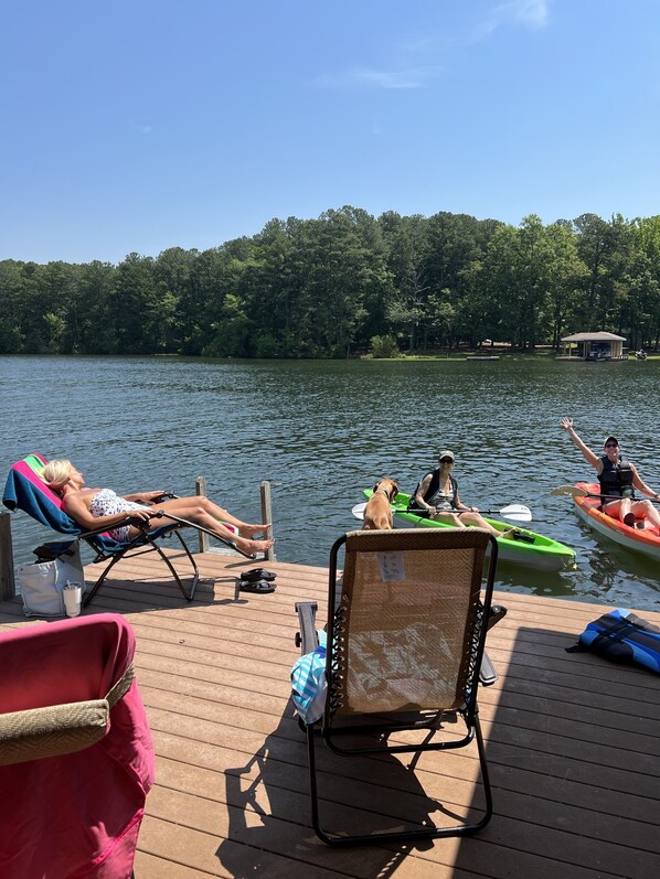 A wooden deck with lounge chairs, a small boat, and a person in a kayak.