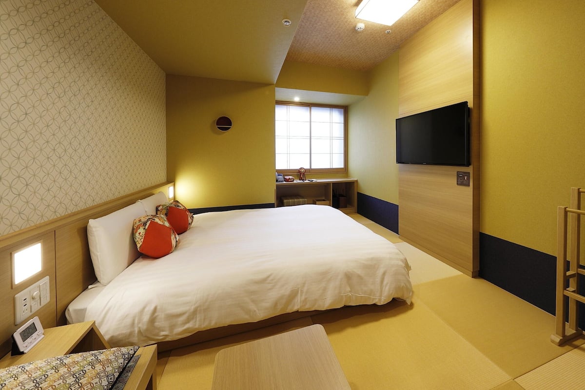 A hotel room with a bed, bedside table, and a TV mounted on the wall.