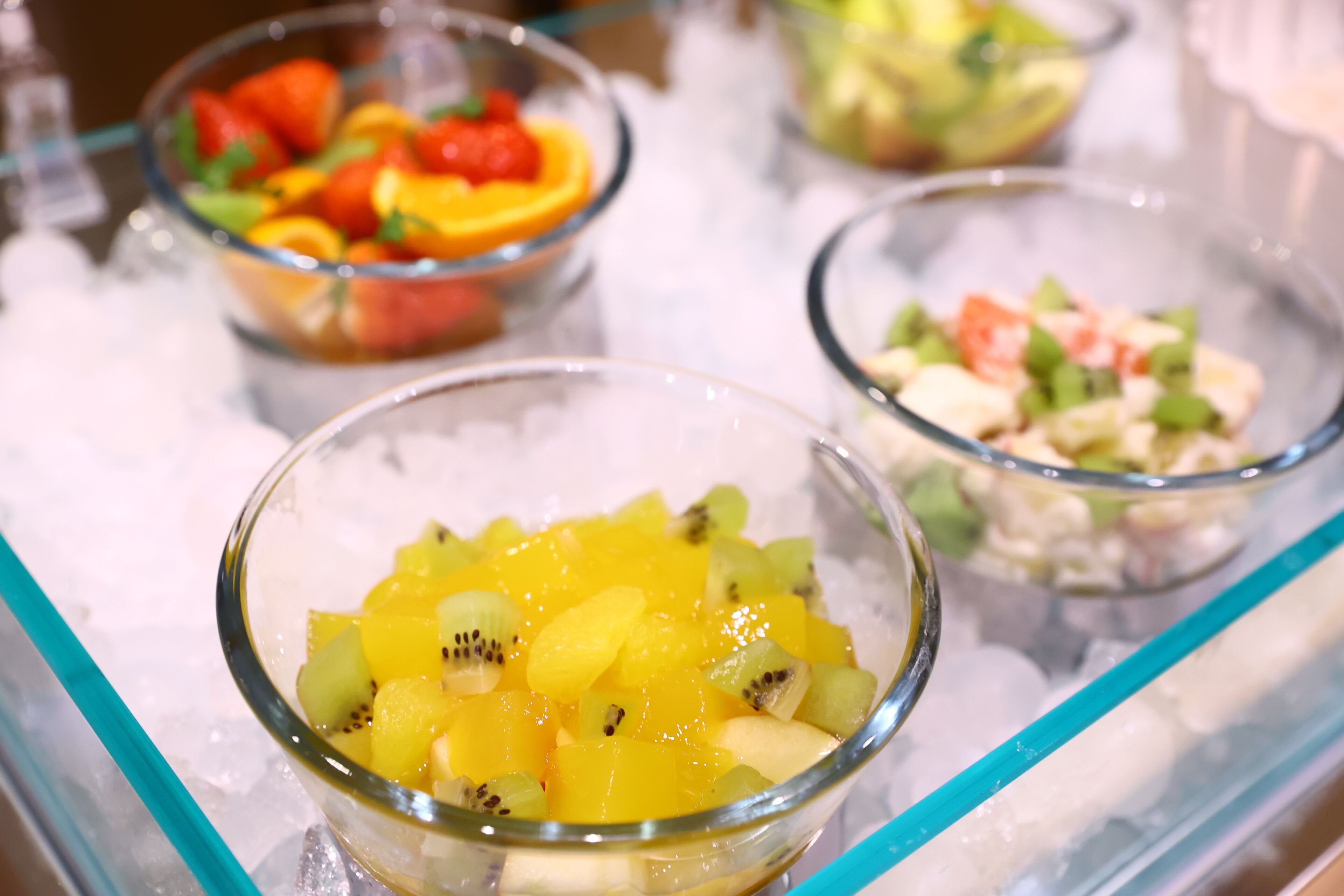 Drei Schalen mit Obstsalat auf einer Glasplatte mit Eis.