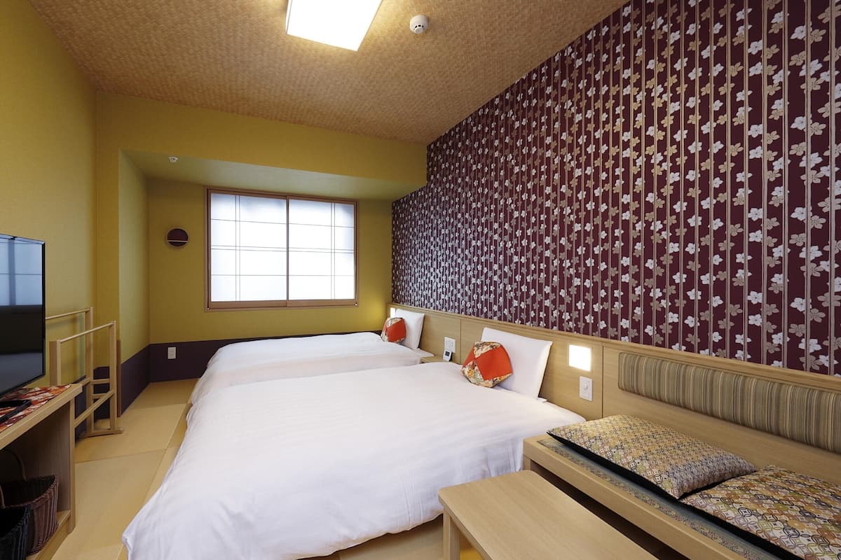 A hotel room with two beds, a sofa, a TV, and a window.