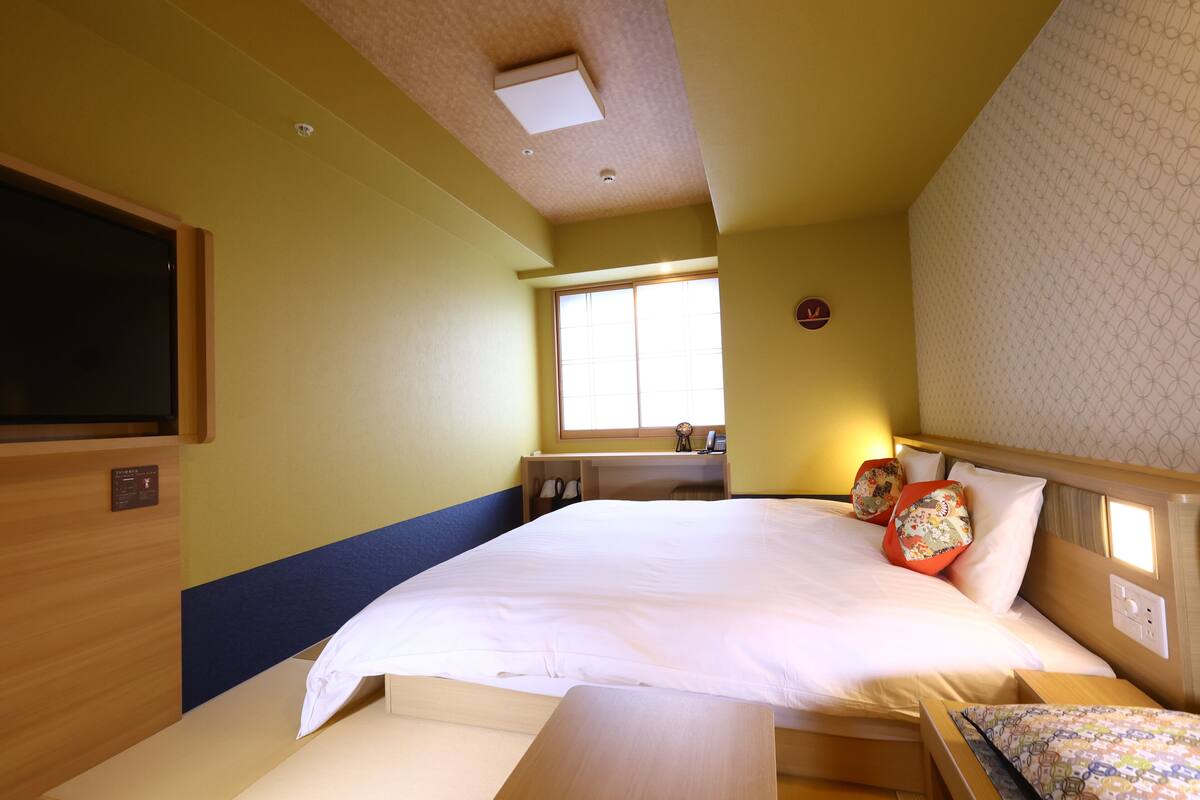 A hotel room with a large bed, a desk, and a window with blinds.