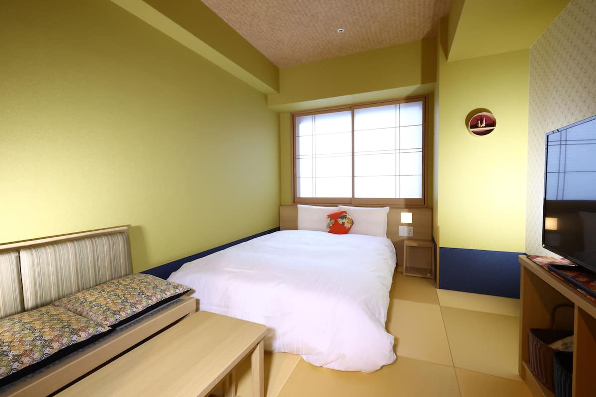 A hotel room with a bed, a small table, a TV, and a window.