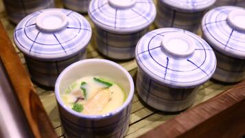 A row of ceramic bowls with lids, some containing food, placed on a bamboo mat.