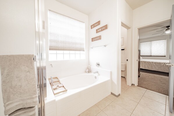 A modern bathroom with a freestanding bathtub, a towel rack, and a window with blinds.