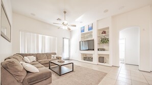 Ein geräumiges Wohnzimmer mit einem beigefarbenen Sofa, einem Couchtisch und einem Deckenventilator.