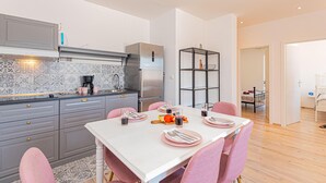 Una cocina moderna con armarios grises, un refrigerador de acero inoxidable y un comedor con una mesa blanca y sillas rosadas.