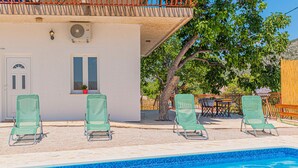 Un área junto a la piscina con cuatro sillas reclinables verdes, una mesita y una planta en maceta.