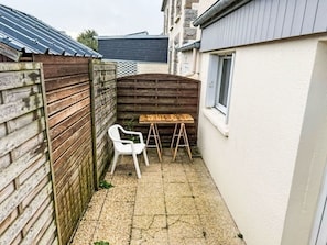 A small outdoor patio area with a wooden table, a white plastic chair, and a ladder.