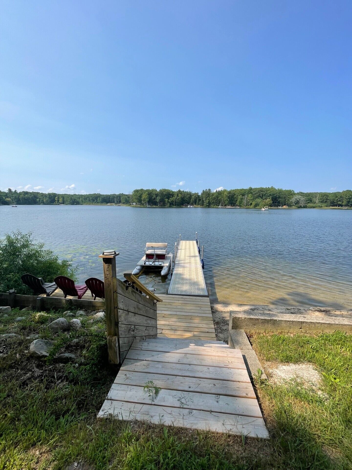 Une jetée en bois s’étendant sur un lac paisible, avec des chaises et une petite barque amarrée à son extrémité.