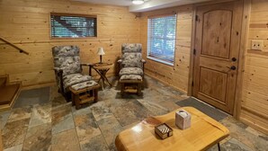 A cozy room with wooden walls, two armchairs, a small table, and a door. - Beautiful 2 BR Lakefront Cabin on Long Lake, Harrison Mi (Harrison)