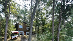 A wooden cabin with a stone staircase leading to a deck, surrounded by dense forest. - Beautiful 2 BR Lakefront Cabin on Long Lake, Harrison Mi (Harrison)