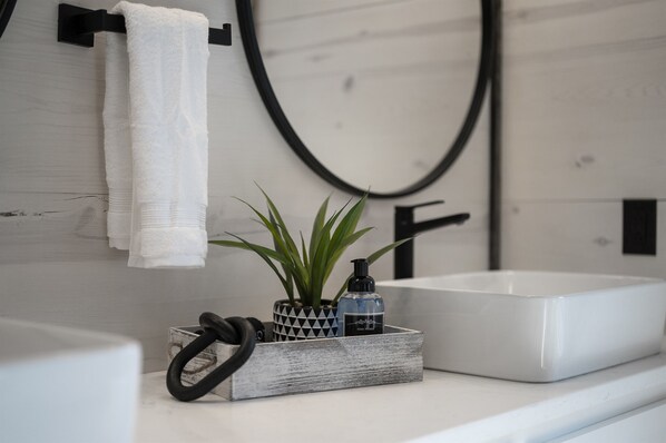 A bathroom with a white sink, a towel hanging on a black towel bar, a potted plant, and a black ring.