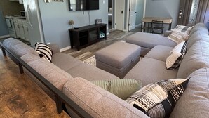 A spacious living room with a large sectional sofa, a flat-screen TV, and a dining area with a table and chairs. - Peaceful lake retreat (Coldwater)