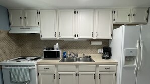 A kitchen with white cabinets, a stove, a microwave, a sink, and a refrigerator. - Peaceful lake retreat (Coldwater)