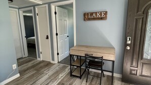 A room with a wooden dining table, two chairs, a gray sofa, and a door with a 'LAKE' sign. - Peaceful lake retreat (Coldwater)