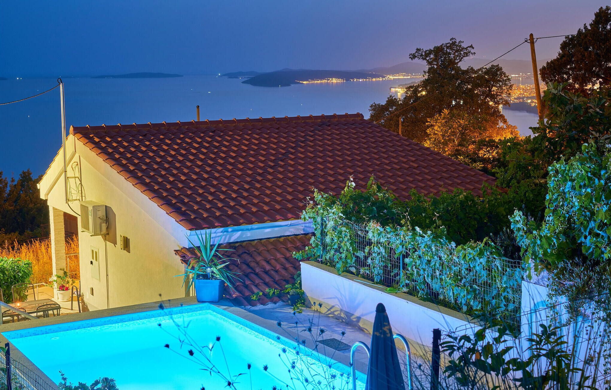 A house with a swimming pool, a red-tiled roof, and a view of a body of water at dusk.