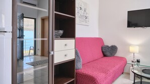 Et moderne soveværelse med glasdør til en balkon, en lyserød sofa og et fladskærms-tv ophængt på væggen.