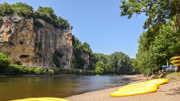 Ein Fluss mit einer felsigen Klippe und gelben Kanus am Ufer.