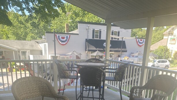 A covered outdoor patio with wicker furniture, a glass-top table, and a red and beige patterned rug.