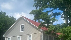 A two-story house with a red roof, a porch with a railing, and a small garden area.