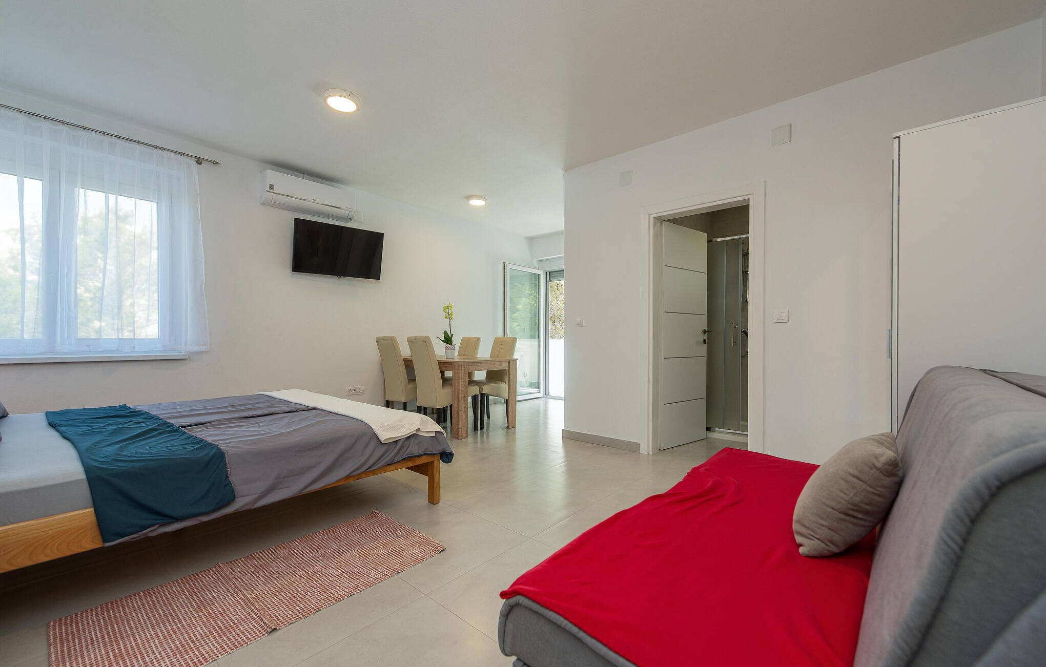 A modern bedroom with two beds, a dining area, and a bathroom.