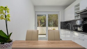 Eine moderne Küche mit Essbereich, einer Kaffeemaschine und Blick auf Bäume durch eine Glastür.