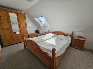 A bedroom with a wooden bed, a wardrobe, a desk, a chair, and a skylight. - Ferienhaus Wittmunder Str. 37 A (Wittmund)