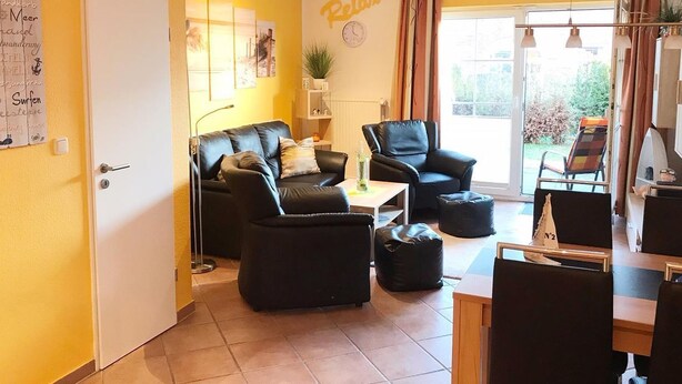 A living room with a sofa, two armchairs, a coffee table, and a dining area with a table and chairs. - Vacation home Am Kurzentrum 26 No. 2 (Wittmund)
