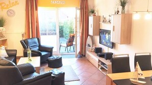 A living room with a sofa, chairs, a coffee table, a TV, and a small table with a model ship. - Vacation home Am Kurzentrum 26 No. 2 (Wittmund)