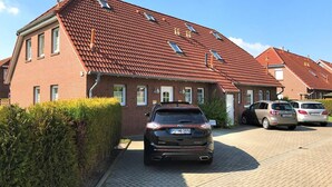 A residential building with a red-tiled roof, multiple windows, and a paved driveway. - Vacation home Am Kurzentrum 26 No. 2 (Wittmund)