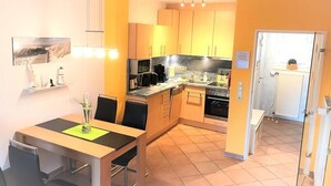 A compact kitchen with a dining area, featuring a tiled floor, wooden cabinets, and a small refrigerator. - Vacation home Am Kurzentrum 26 No. 2 (Wittmund)