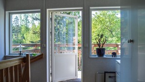 Une pièce avec un banc en bois, une plante en pot et une vue sur une terrasse en bois et des arbres.