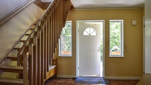 Un escalier en bois mène à une porte dotée d’une petite fenêtre, d’une fenêtre plus grande et d’un paillasson à l’entrée.