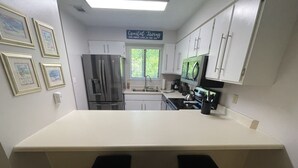 A kitchen with white cabinets, a stainless steel refrigerator, a stove, and two black bar stools. - Gorgeous, Family-Friendly Portside Resort in PCB - Walking Distance to the Beach (Panama City)