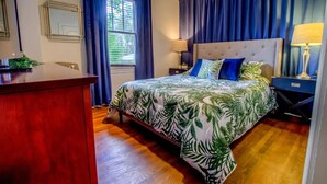 Ein Schlafzimmer mit Bett, Nachttisch, Schreibtisch, Fenster und Vorhängen.
