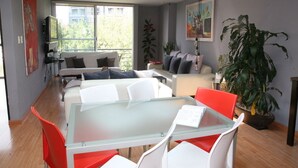 Un salón moderno con una mesa de vidrio, sillas blancas y rojas, un sofá y una planta grande en maceta.